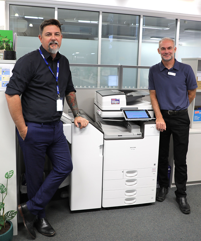 Trees consumed and CO2 produced by paper production has been drastically reduced with the City of Greater Geraldton implementing a swath of changes to its printer fleet. City of Greater Geraldton CEO Ross McKim was impressed to see how simple changes in the office had resulted in a positive effect on paper consumption. “In the 2014-15 financial year the City was consuming almost a staggering 200 trees worth of paper,” he said. “Right now for this financial year we’re hovering at just under 60 trees consumed – an incredible reduction that sees not only a stark drop in trees used, but also a massive reduction in CO2 production. “This was made possible by making a few key changes in our offices, such as reducing our printer fleet and introducing swipe card release of documents from the print queue. “We have also made the move to digitise a lot of our paper based processes – a step that businesses of any size can take to reduce paper use,” he added.  According to conservatree.org a single tree will make an estimated 8,333.3 sheets of paper, which equates to 16.67 reams of paper. This change is the latest in the City’s effort to reduce emissions, with solar panels installed on various City buildings and implementation of various water saving measures that saw the Aquarena claim a Waterwise accolade in 2020. Council declared a Climate Emergency in 2020, committing the City of Greater Geraldton to develop a Corporate Energy Plan that aims to transition City operations to a net zero carbon position by 2030. ENDS:  Picture Caption: Manager ICT Services Dennis Duff and Senior Systems Administrator Dean Nelmes with a swipe card release printer.